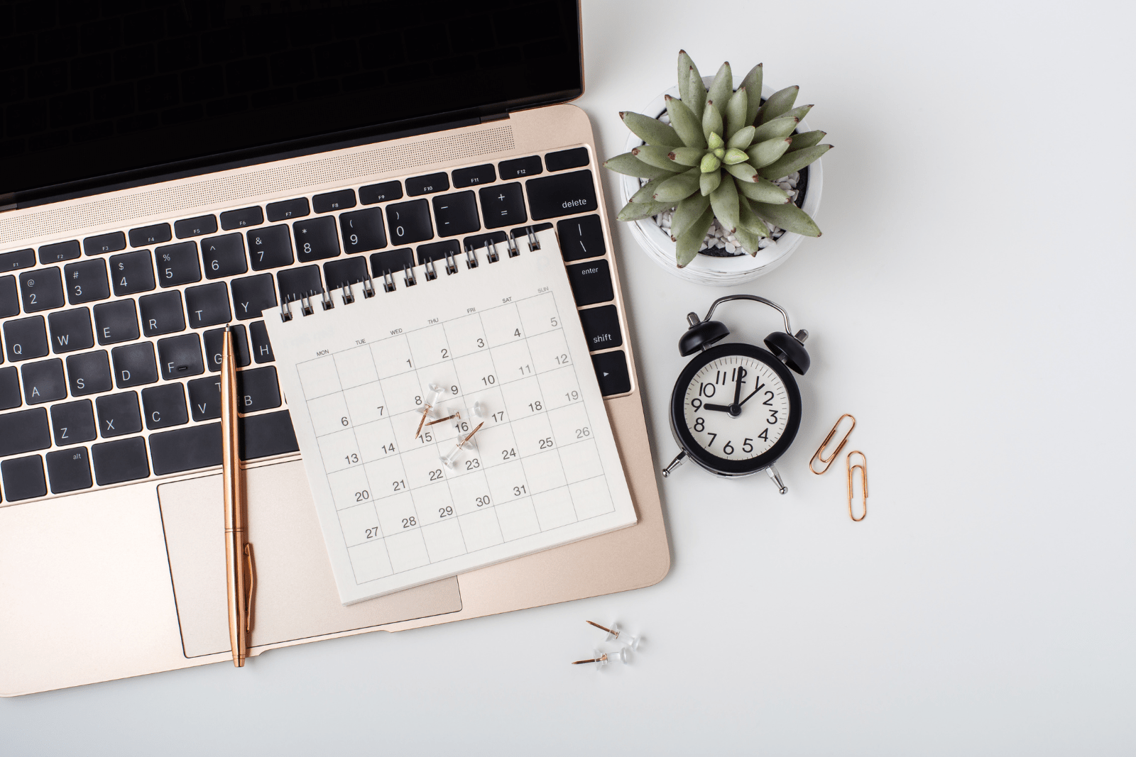 Laptop and calendar with pen and clock next to them on the desk